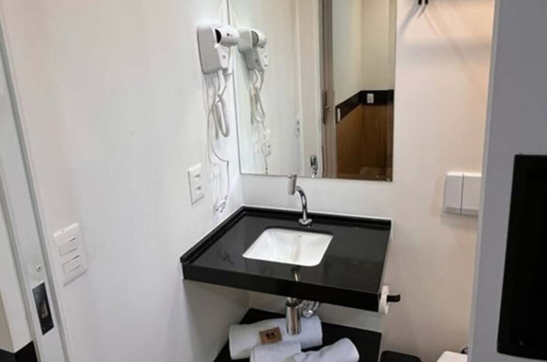 A bathroom with a black countertop sink, a mirror, and a hairdryer mounted on the wall.