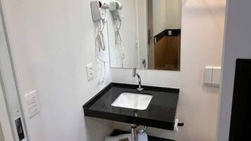 A bathroom with a black countertop sink, a mirror, and a hairdryer mounted on the wall.