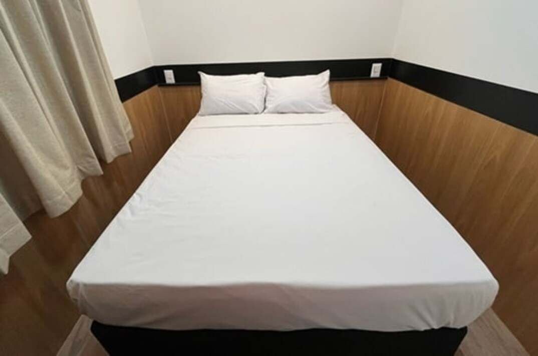 A single bed with a white mattress and pillows, a wooden headboard, and a beige curtain.