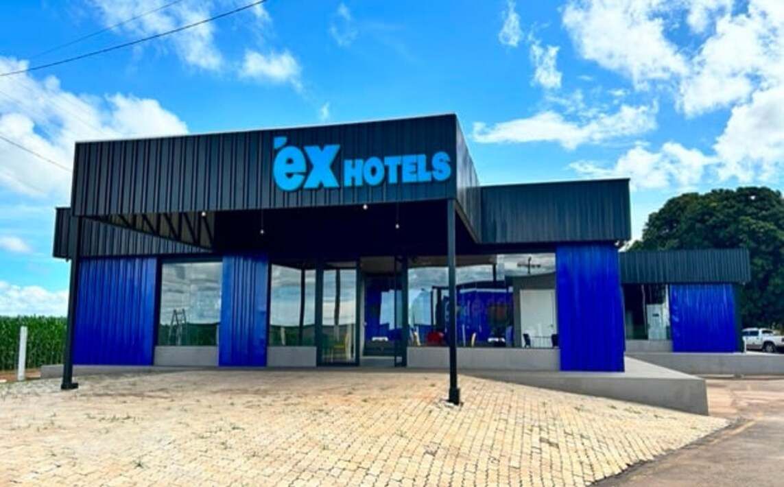 A modern hotel with a prominent 'ex hotels' sign, a covered entrance, and a paved driveway.