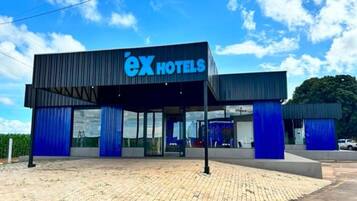 A modern hotel with a prominent 'ex hotels' sign, a covered entrance, and a paved driveway.