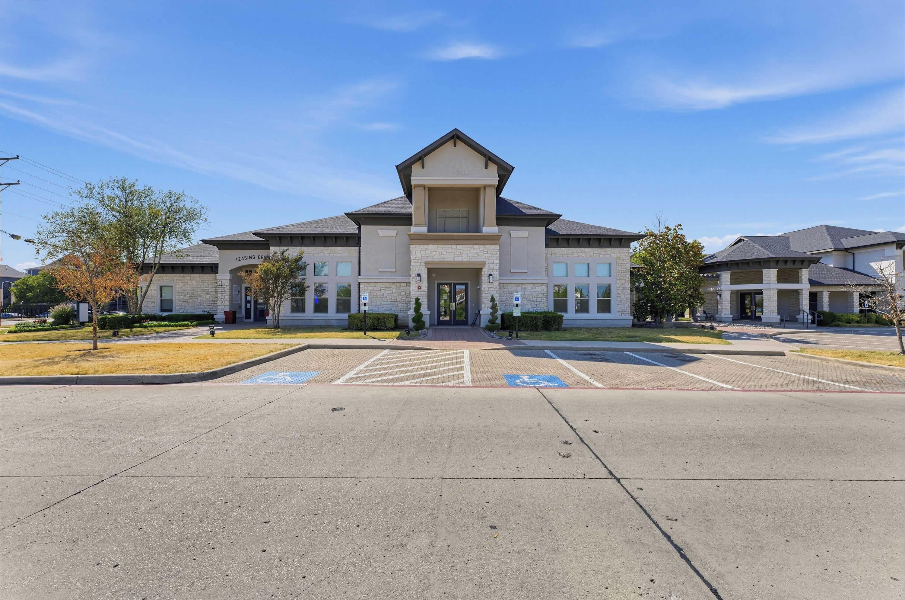 A LEASING CENTER with a stone facade, a central entrance, and a parking lot with marked handicapped spaces.