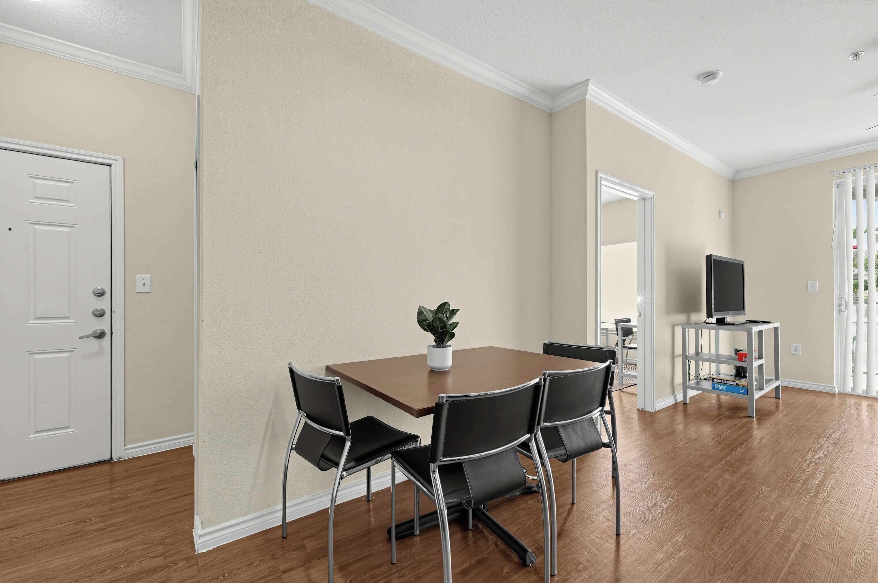A dining area with a table, chairs, a potted plant, and a television on a stand.