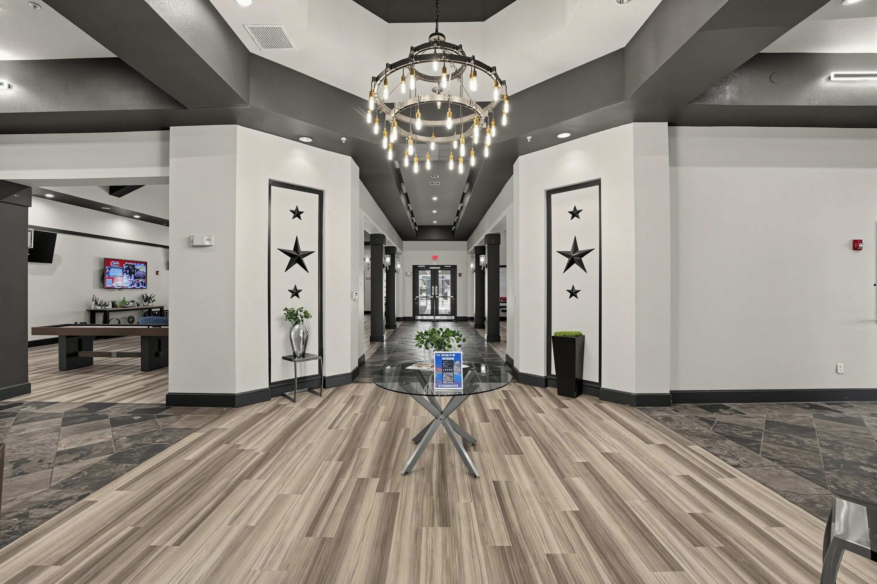 A hotel lobby with a modern chandelier, star decorations on the walls, a reception desk, and a digital screen.
