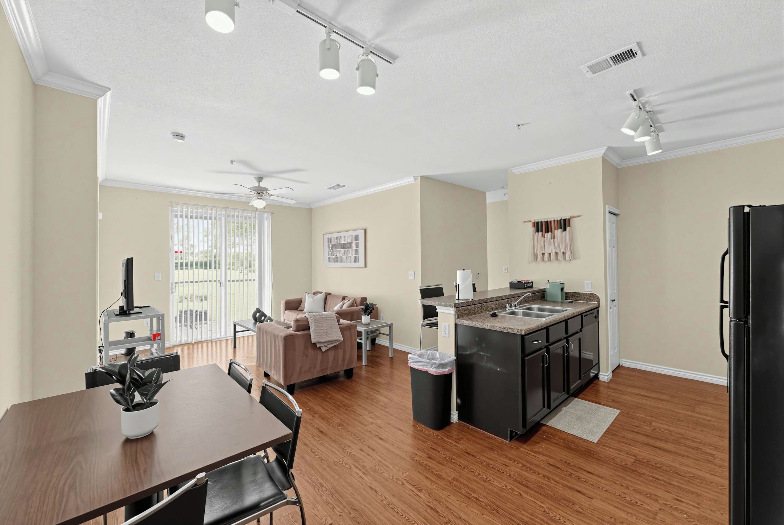 A modern kitchen with a central island, a dining area with a table and chairs, and a living room with a sofa and a ceiling fan.