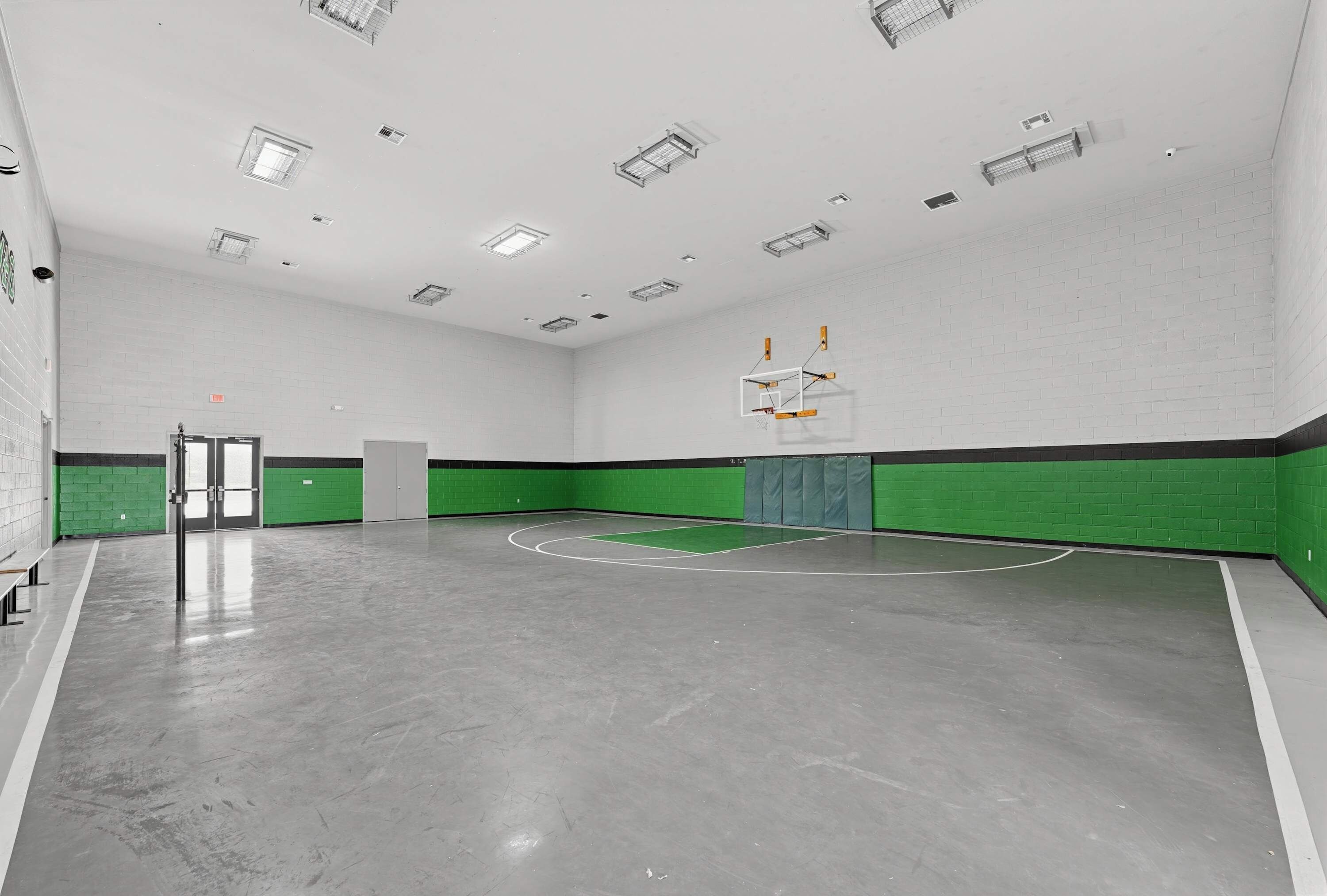 A basketball court with a hoop, a door, and a bench.