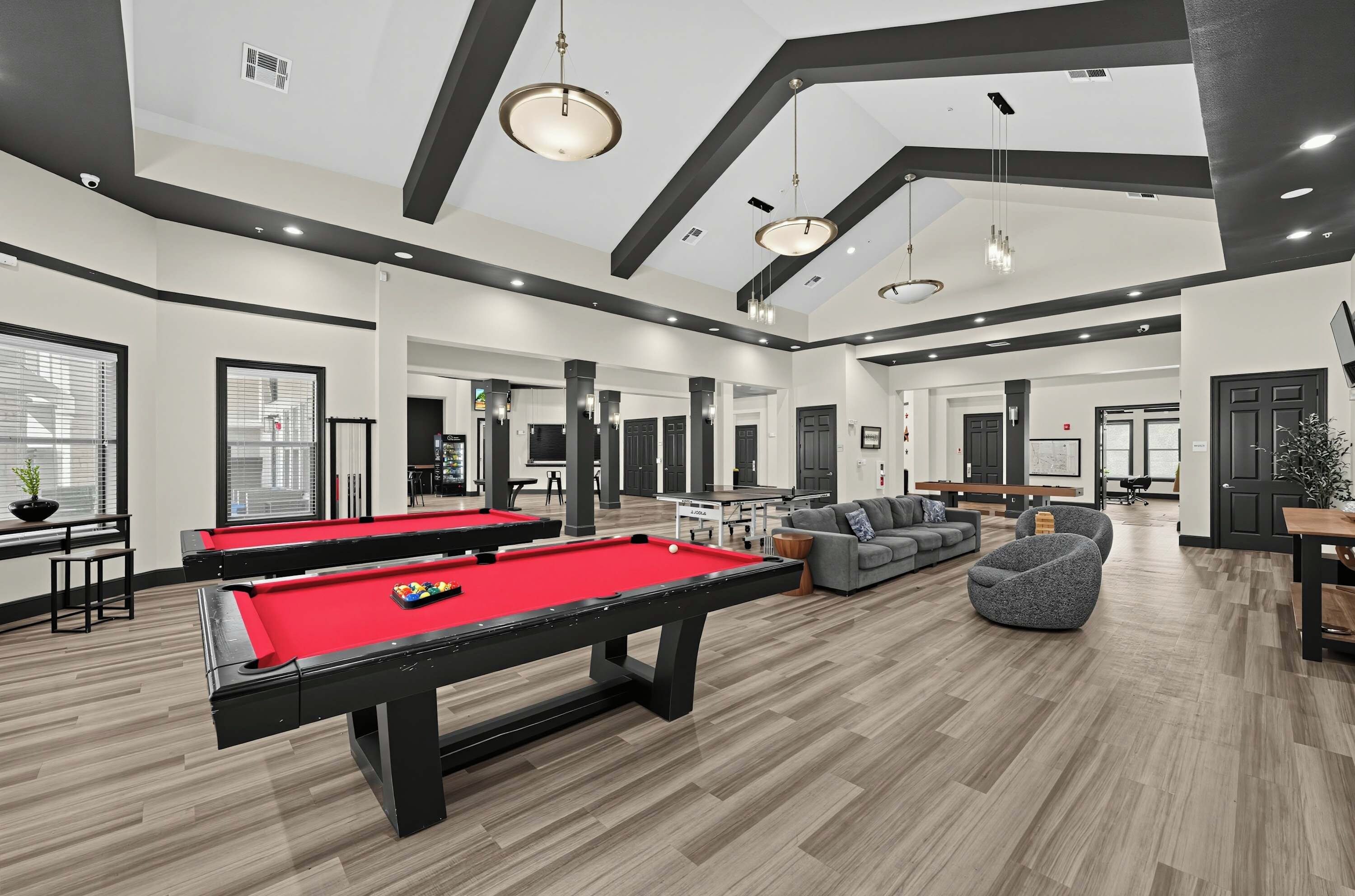 A modern indoor recreational area with pool tables, seating, and a high ceiling with exposed beams.