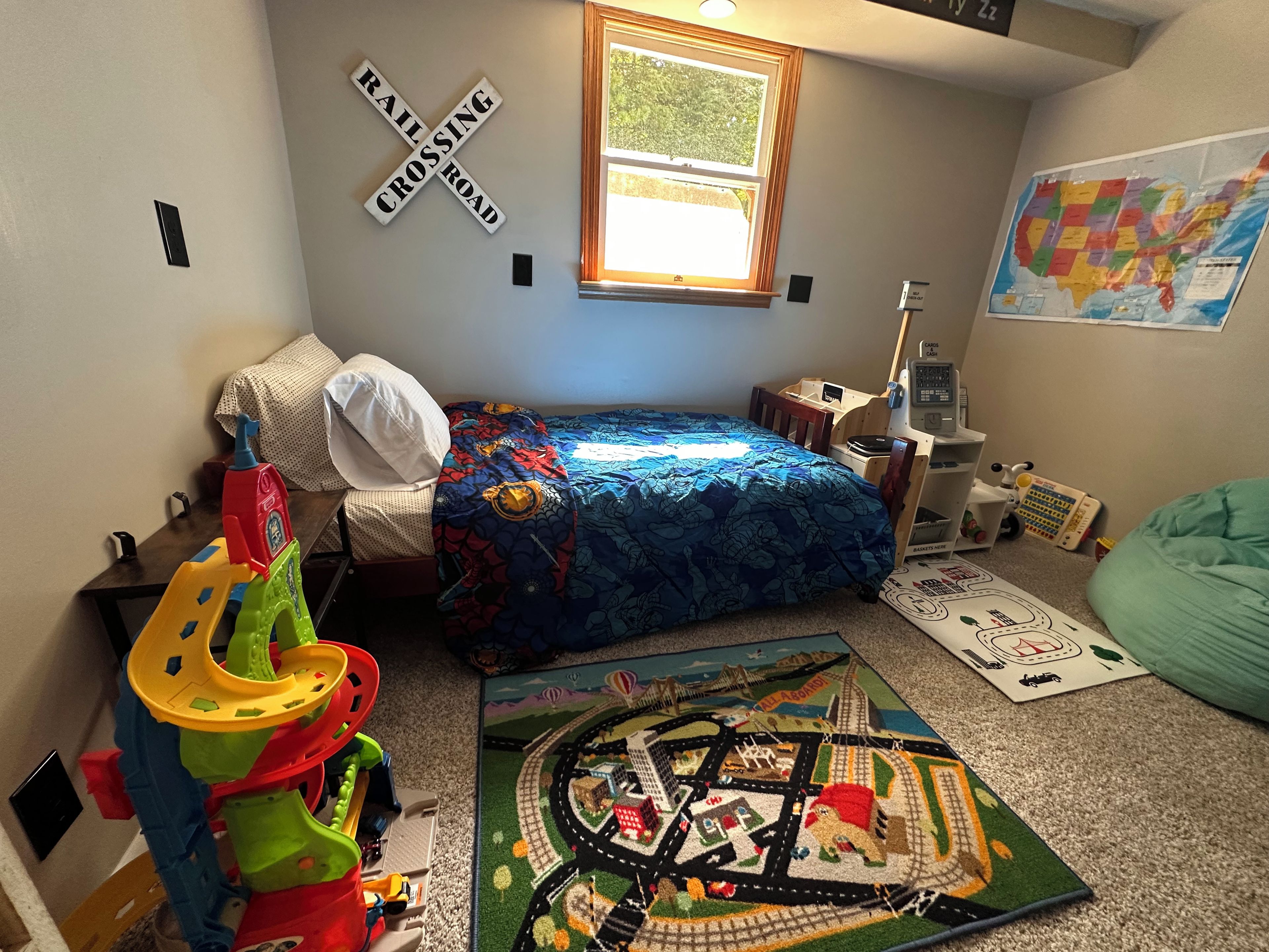 A child's bedroom with a bed, toys, a train set, and a map on the wall.