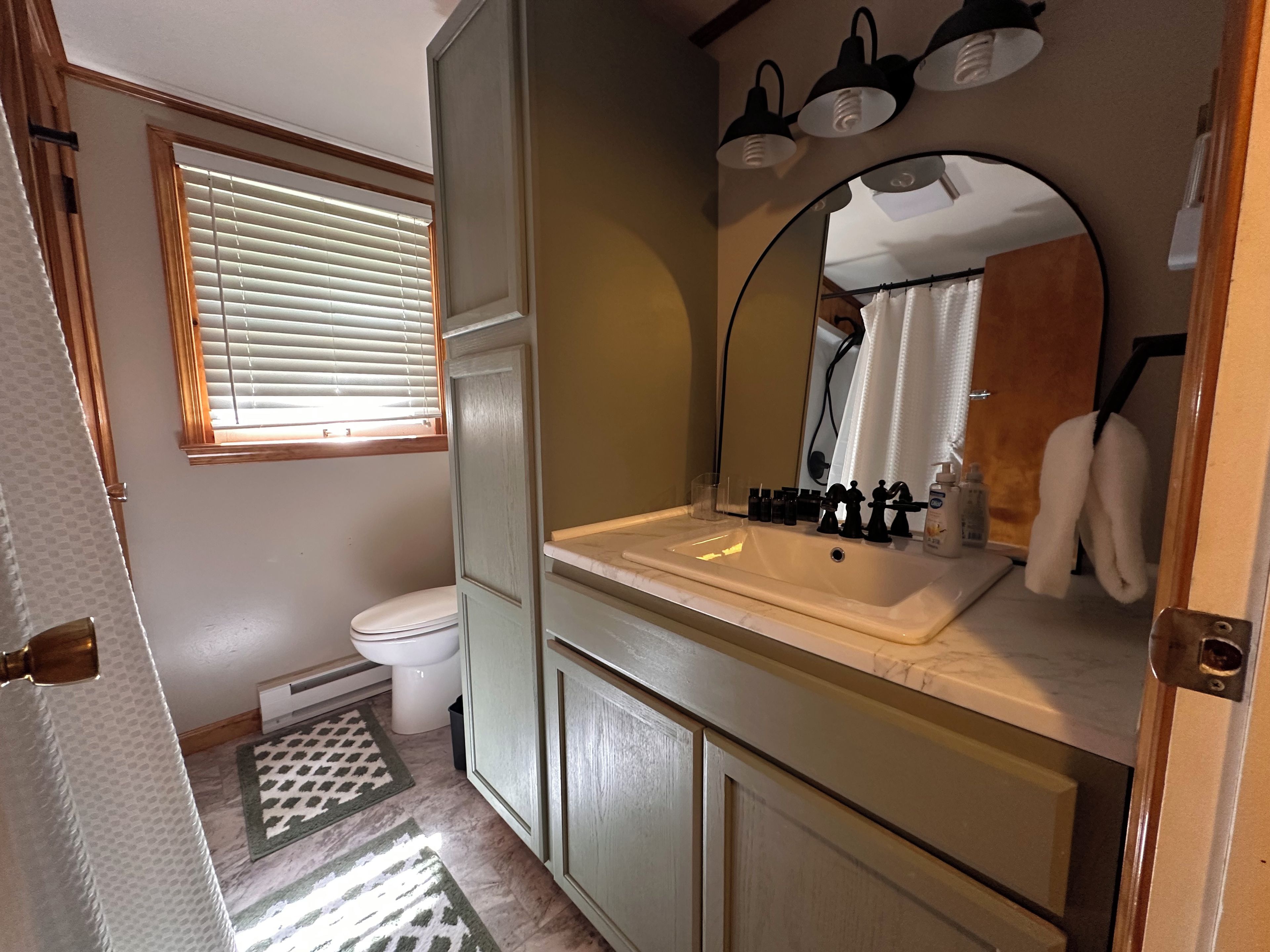 A bathroom with a toilet, sink, mirror, and towel rack.