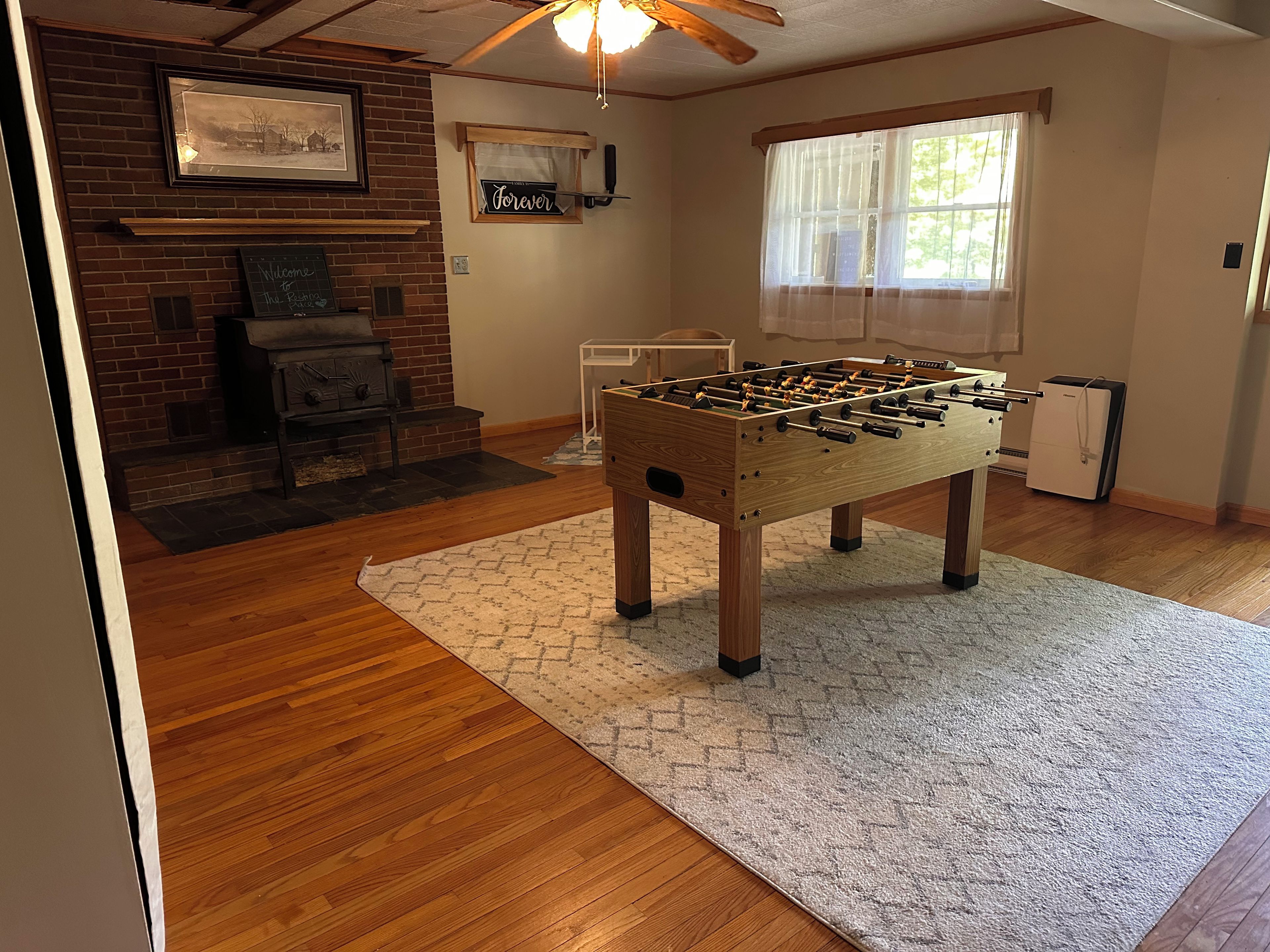 A room with a foosball table, a fireplace, and a window with sheer curtains.