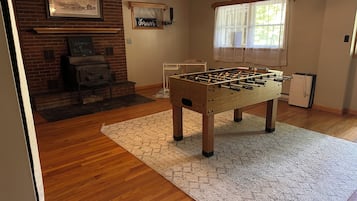 A room with a foosball table, a fireplace, and a window with sheer curtains.