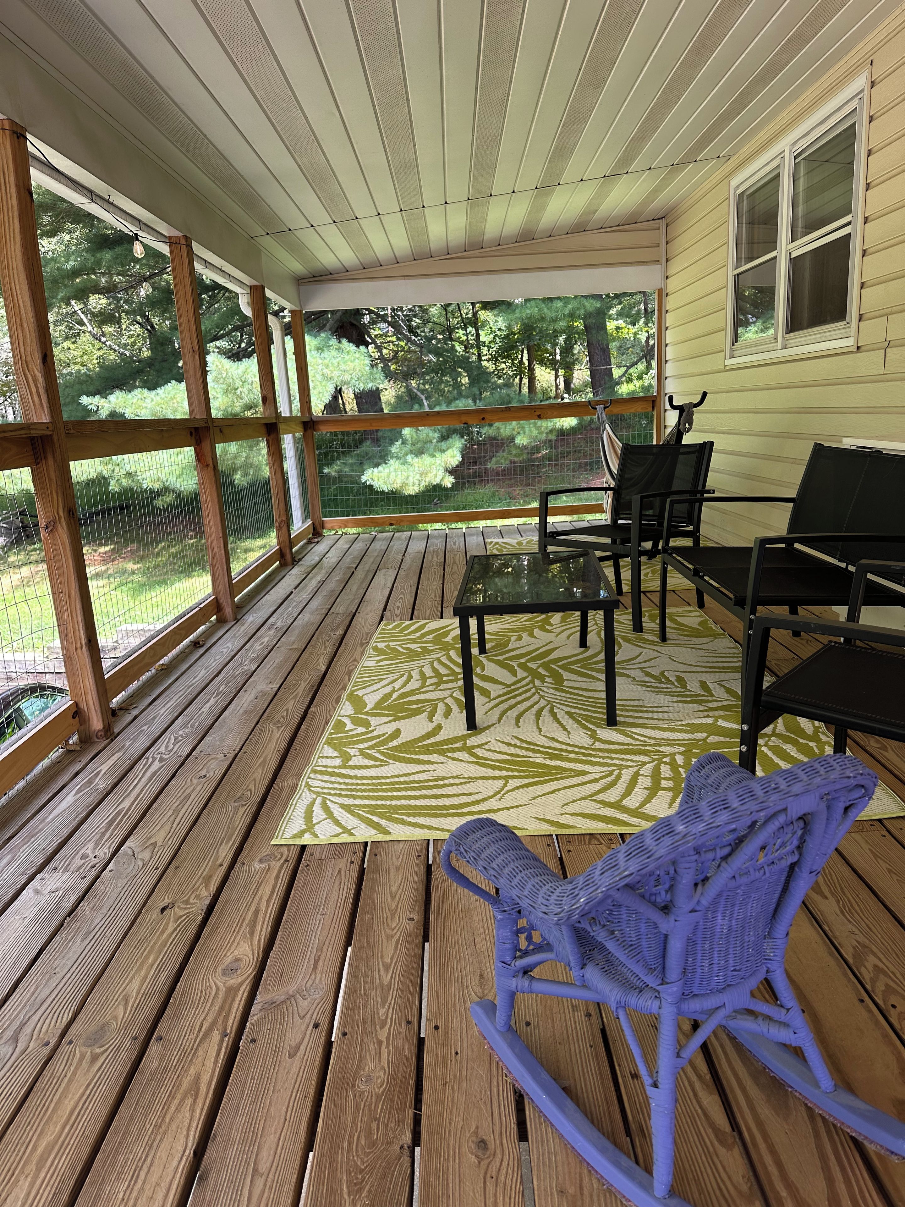 A covered porch with a wooden floor, a patterned rug, and outdoor furniture including a rocking chair and chairs.