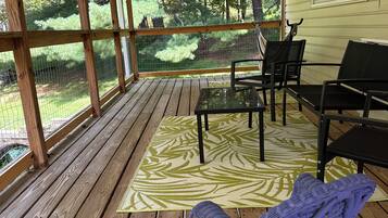 A covered porch with a wooden floor, a patterned rug, and outdoor furniture including a rocking chair and chairs.