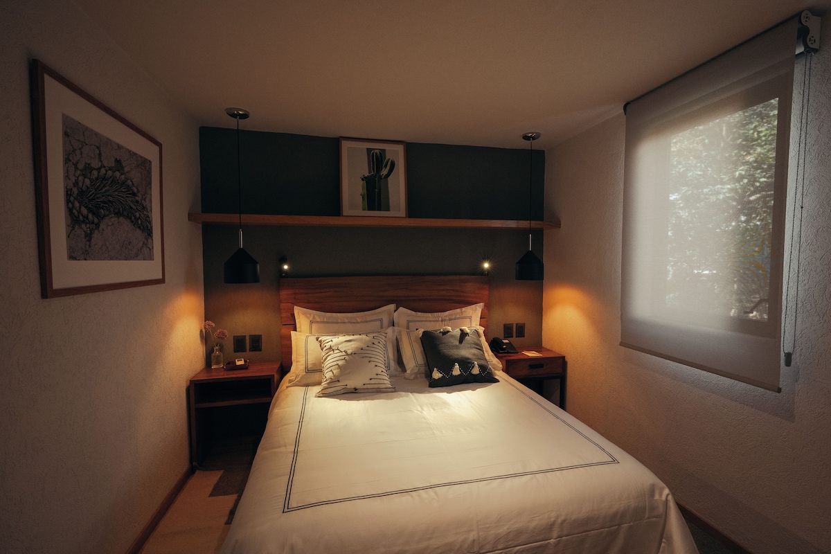 A neatly made bed with a headboard, bedside tables, and a window with natural light.