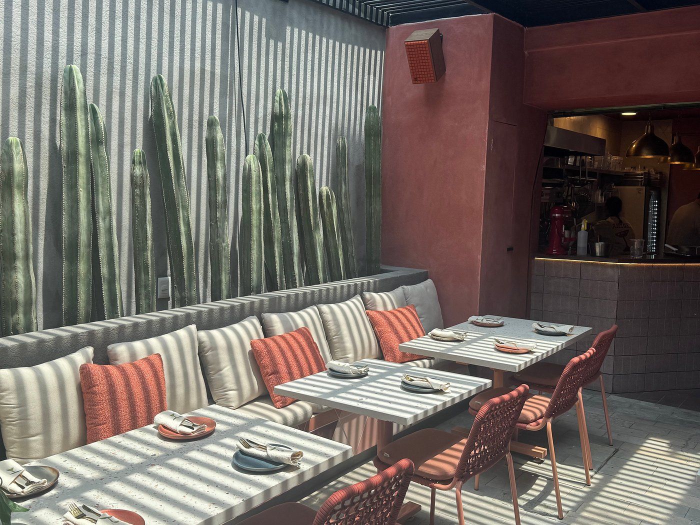 An outdoor seating area with a cactus wall, cushioned seating, and tables with chairs.
