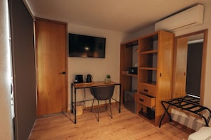 A compact room with a wooden desk, a chair, a small table with a kettle, a microwave, and a built-in wardrobe. - CASA JUMI (Guadalajara)