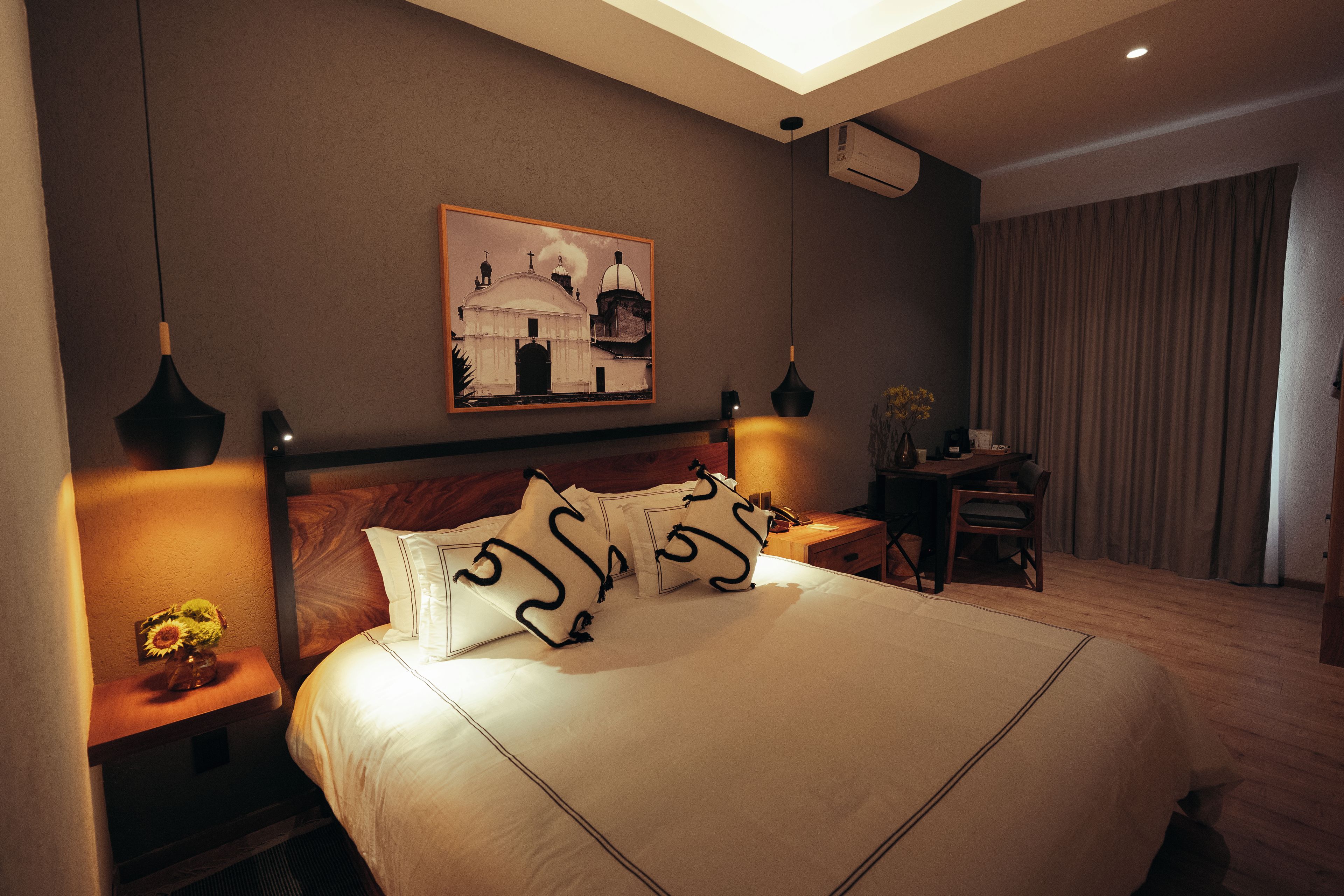 Habitación de hotel con una cama grande, lámparas de noche, un escritorio y un cuadro en la pared.