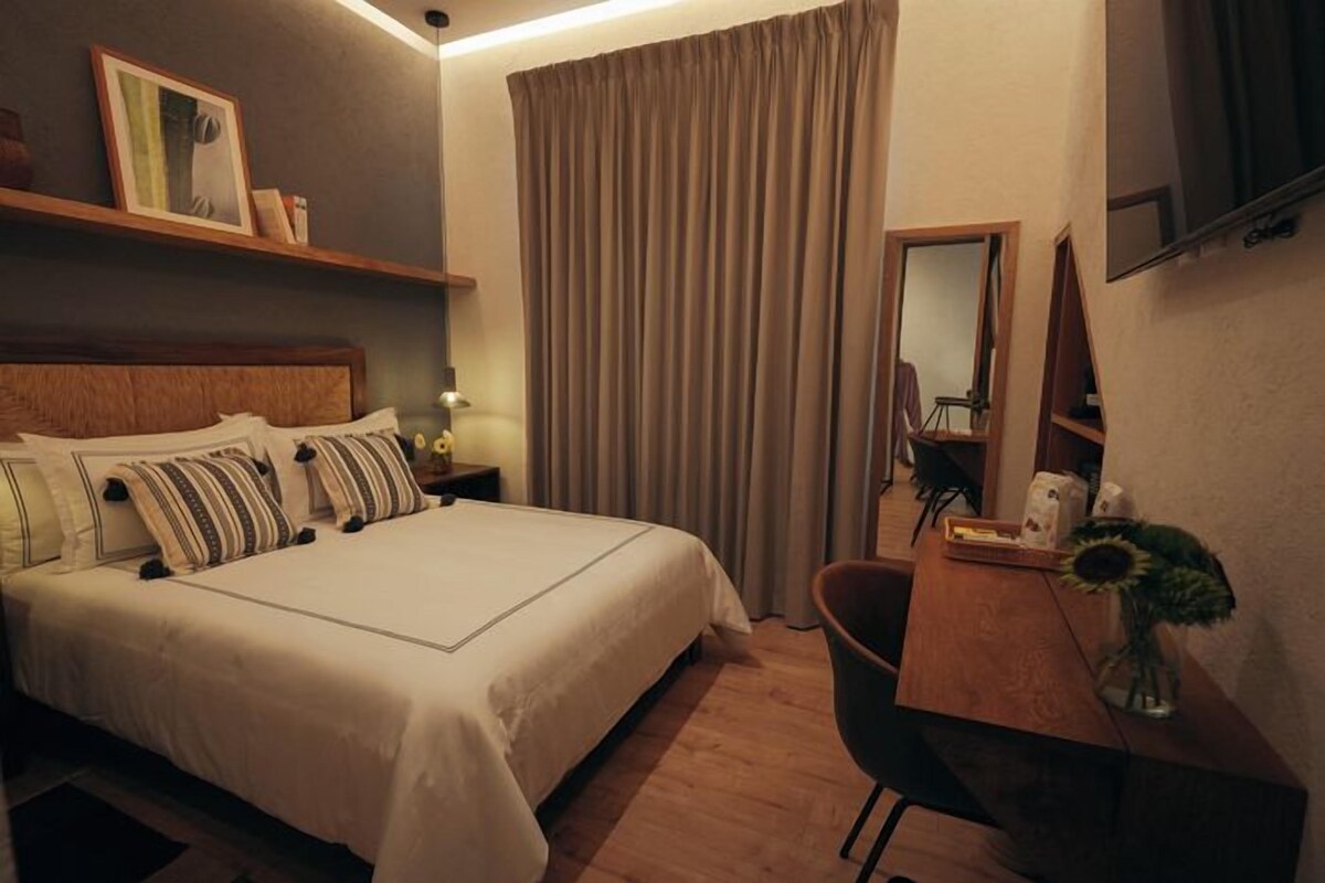A hotel room with a bed, a desk, a chair, a mirror, and a television.