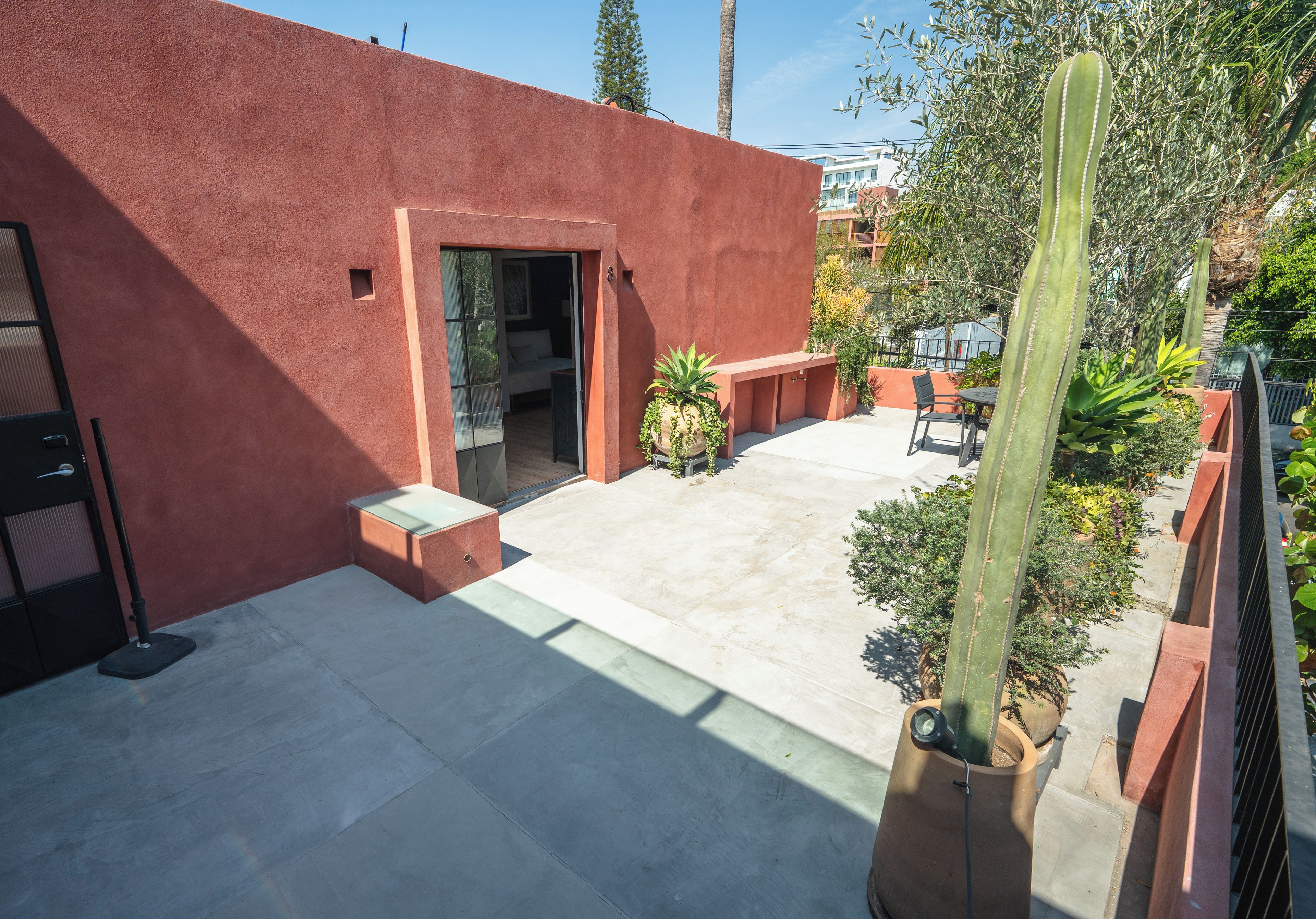 Un edificio moderno con fachada roja, un patio con asientos y una planta de cactus.