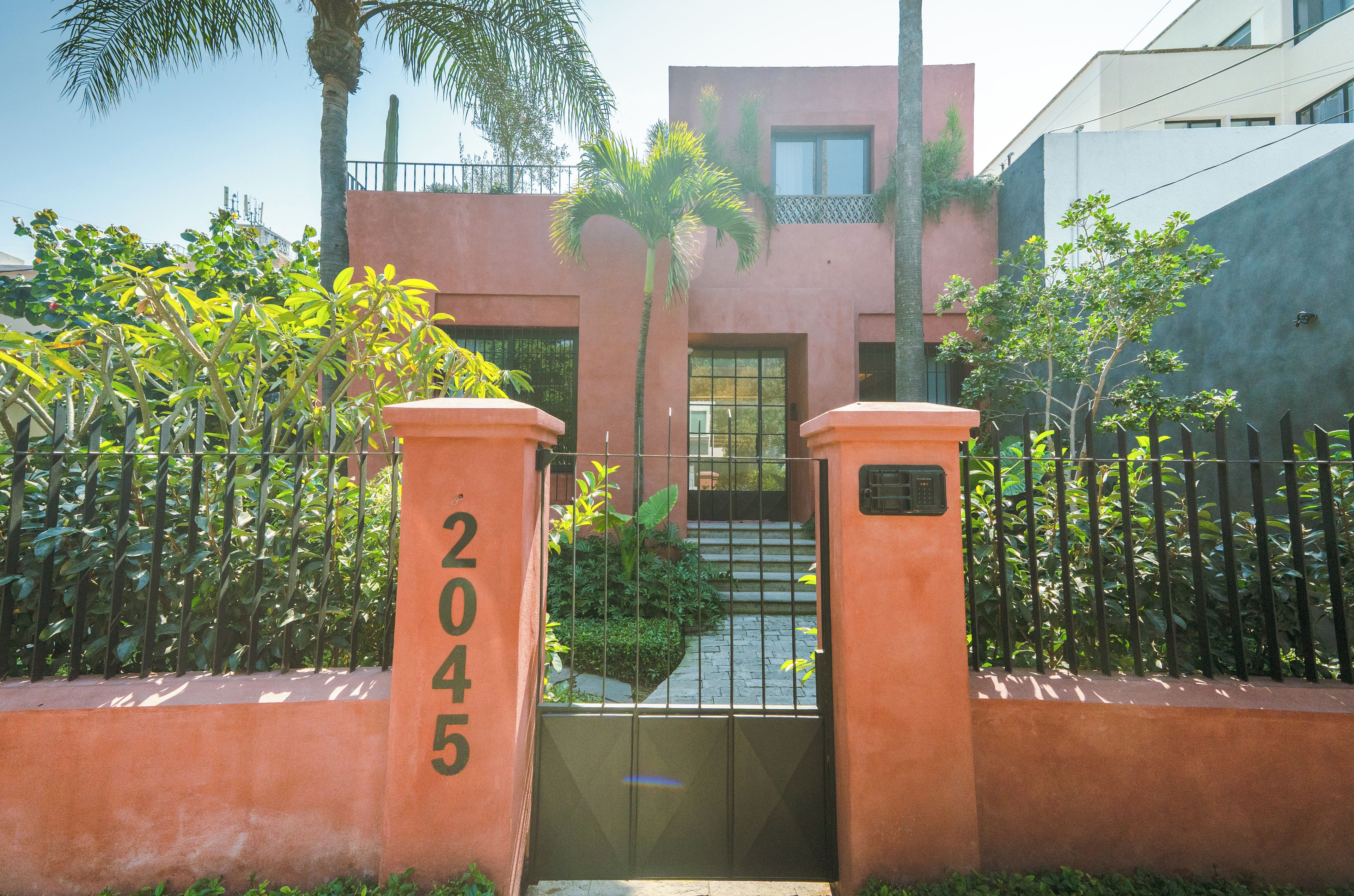 A gated entrance with a number sign, a staircase leading to a building, and surrounding greenery.