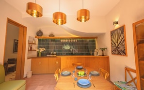 A dining area with a wooden table set for four, a kitchen with a green-tiled backsplash, and pendant lighting. - CASA JUMI (Guadalajara)