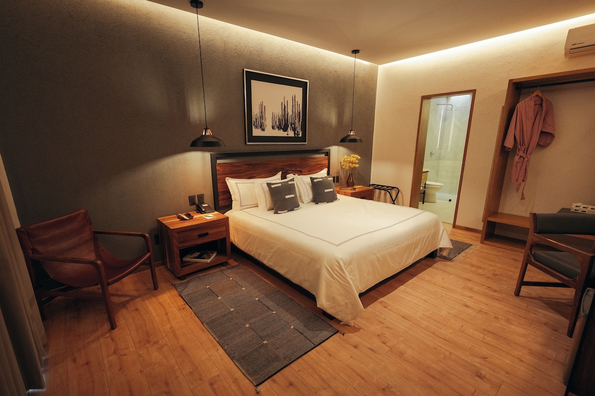 A neatly arranged bedroom with a large bed, bedside tables, a chair, and a shower area.