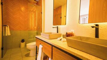 Un baño con piso de madera en patrón de espiga, inodoro blanco, espejo grande y tocador de madera con encimera beige.