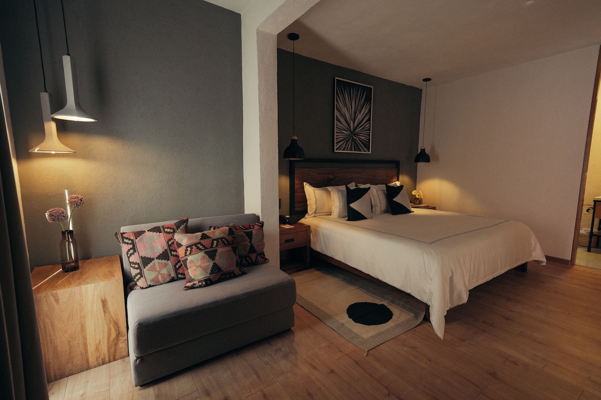 A bedroom with a bed, a sofa, a nightstand, and a wall-mounted light fixture.