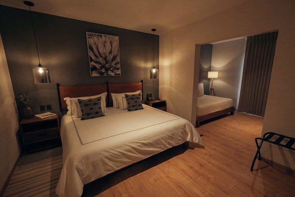 A hotel room with a large bed, bedside tables, a mirror, and a view of the outside.