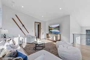 Una sala moderna con sofá, sillones, una mesa de centro y un televisor sobre un mueble de madera.