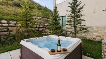 Jacuzzi con una botella de vino y copas, rodeado de un muro de piedra y follaje.