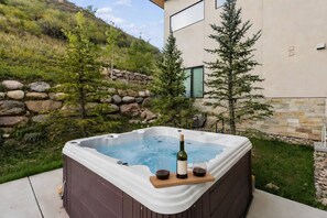 Jacuzzi con una botella de vino y copas, rodeado de un muro de piedra y follaje.