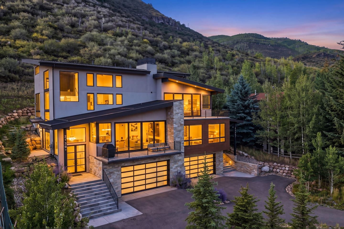 Uma casa moderna de dois andares com garagem, emoldurada por uma paisagem montanhosa.