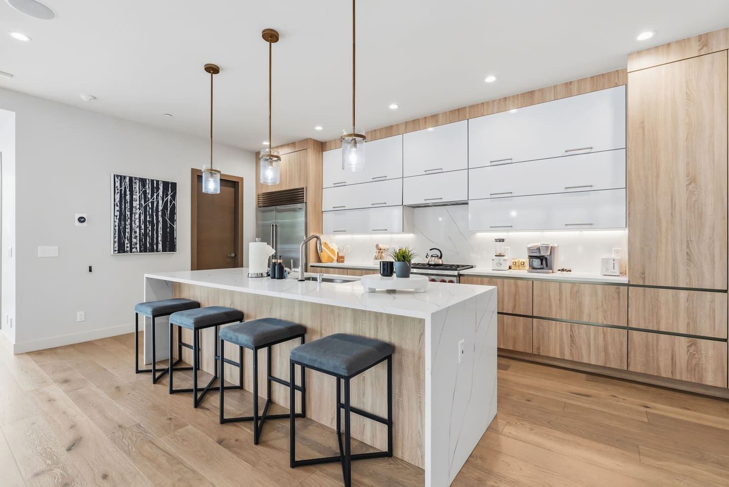 Una cocina moderna con una isla central, taburetes de bar e iluminación colgante.