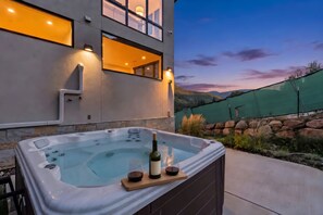 A hot tub with a bottle and glass, set against a modern building with large windows and a view of the mountains. - Luxe West Vail Retreat W/Hot Tub, 8 Mins to Resort (Vail)