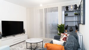 Una sala moderna con un televisor de pantalla plana, una mesa redonda de centro y un sofá gris con cojines naranjas.