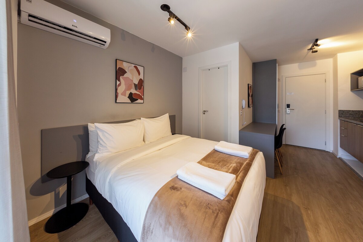 Quarto de hotel moderno com cama, mesa de cabeceira e ar condicionado.