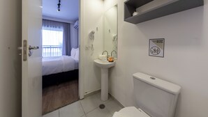Una habitación de hotel con cama, baño con lavabo e inodoro, y espejo.