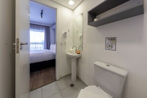 Quarto de hotel com cama, banheiro com pia e vaso sanitário, e um espelho.
