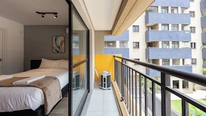 Una habitación de hotel con una cama, un cuadro y vistas a un edificio con balcones.