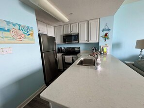 A kitchen with white cabinets, stainless steel appliances, a microwave, and a sink. - Seychelles Beach Resort 1904 (Panama City Beach)