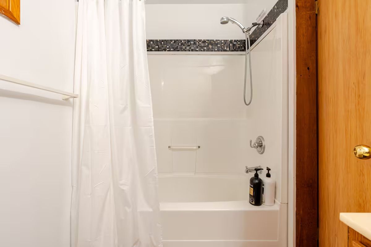 A shower area with a showerhead, a soap dispenser, and a bottle of shampoo.