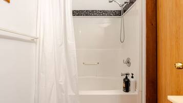A shower area with a showerhead, a soap dispenser, and a bottle of shampoo.