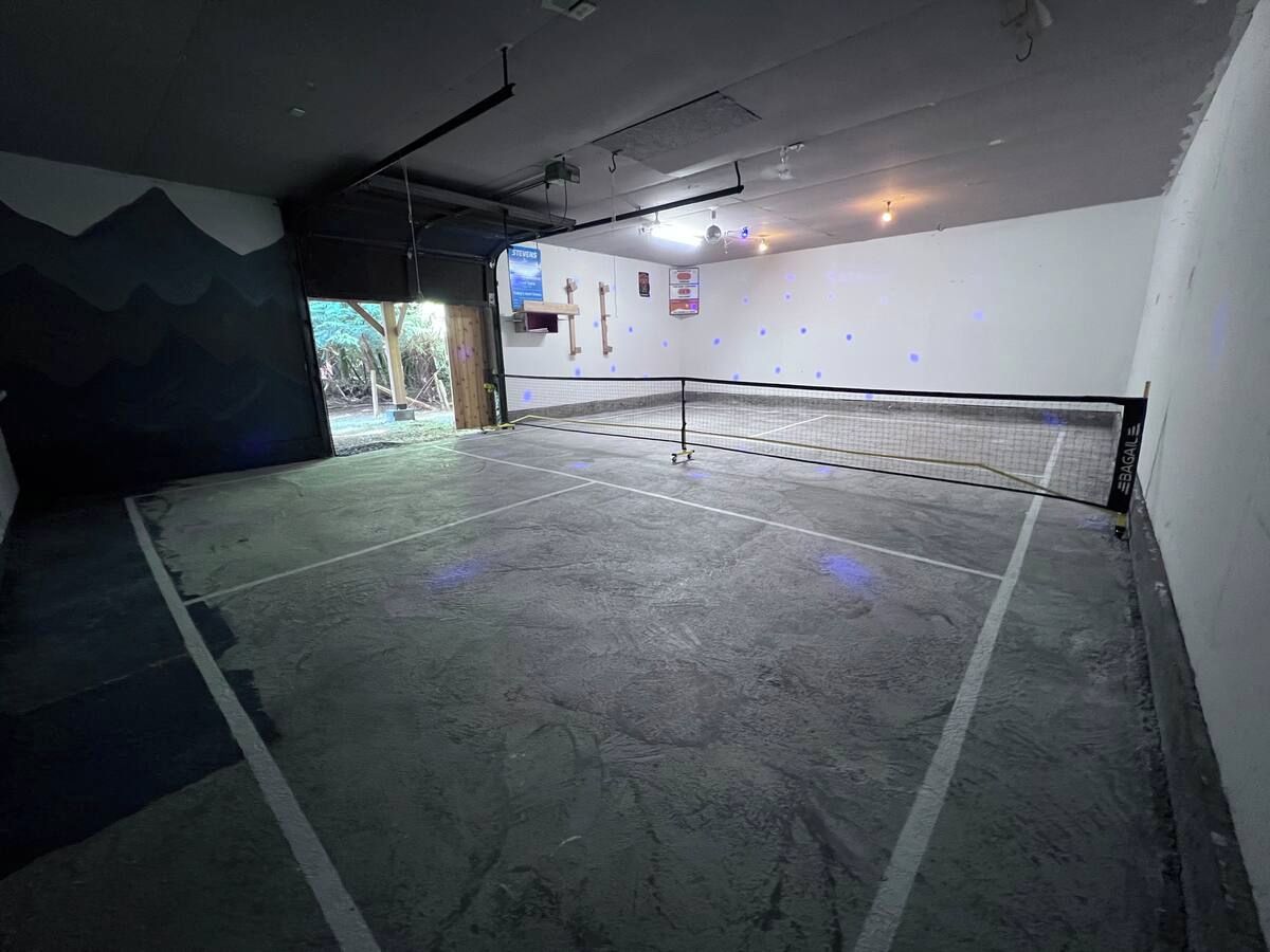 An indoor tennis court with a net, walls, and a ceiling with lights.