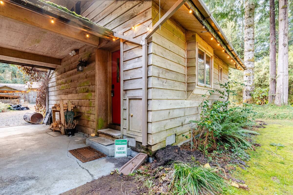 A wooden cabin with a red door, a welcome sign, and a guest parking sign.