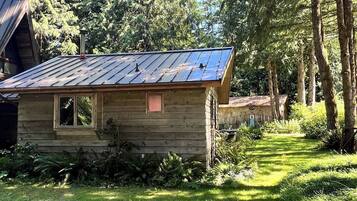 Eine Holzhütte mit Metall-Dach, umgeben von Bäumen und einer grünen Wiese.