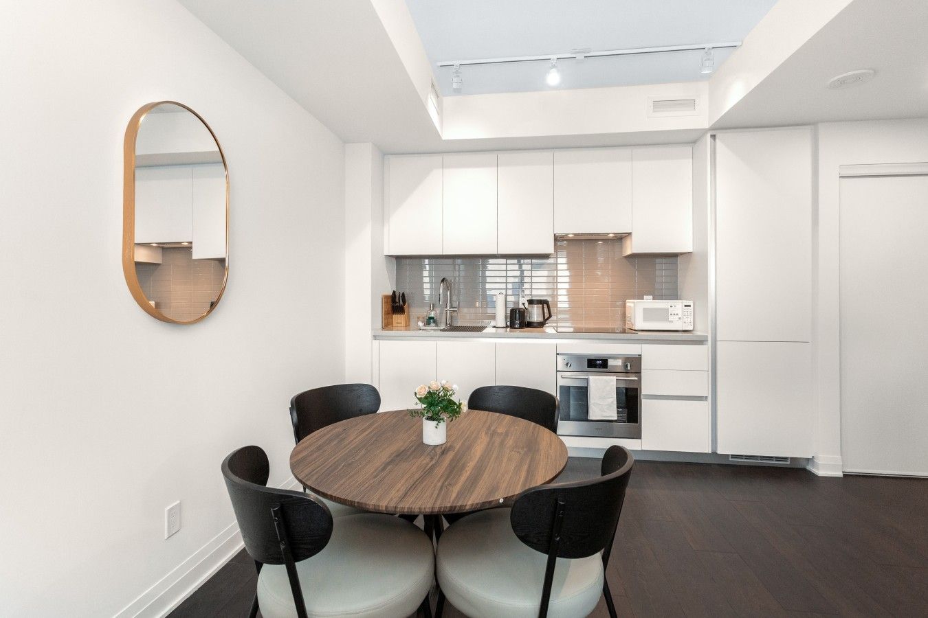 A modern kitchen with white cabinets, a round dining table with four chairs, and a large mirror on the wall.