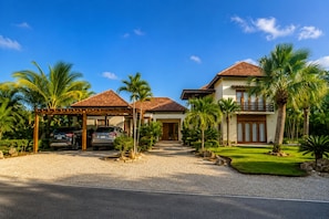 Uma casa de dois andares com garagem coberta, palmeiras e um gramado bem cuidado.