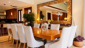 Uma sala de jantar com mesa de madeira, cadeiras estofadas brancas e um espelho grande com moldura de madeira.