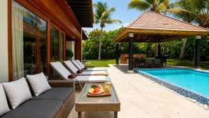 A poolside area with lounge chairs, a table with fruit and drinks, and a covered seating area. - Villa CapCana: 5-Bedroom Villa with Pool, Jacuzzi, Beach, and Golf (Punta Cana)